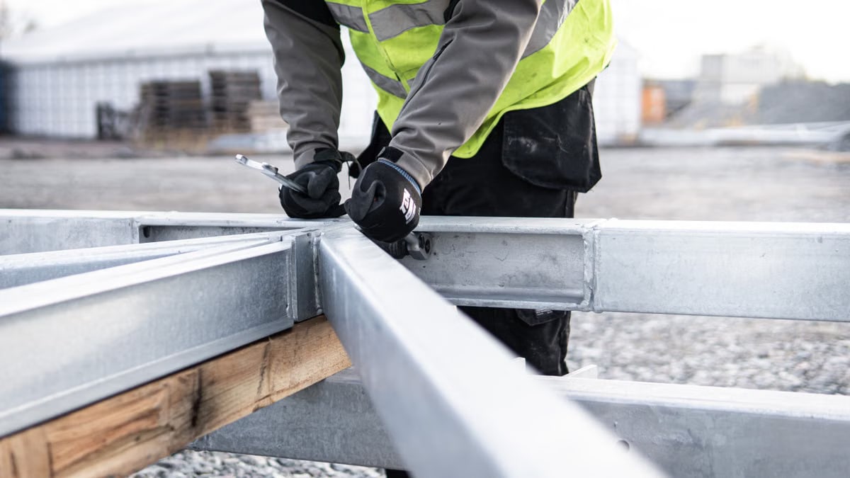 A construction worker adjusting steel beams outdoors for a building framework.